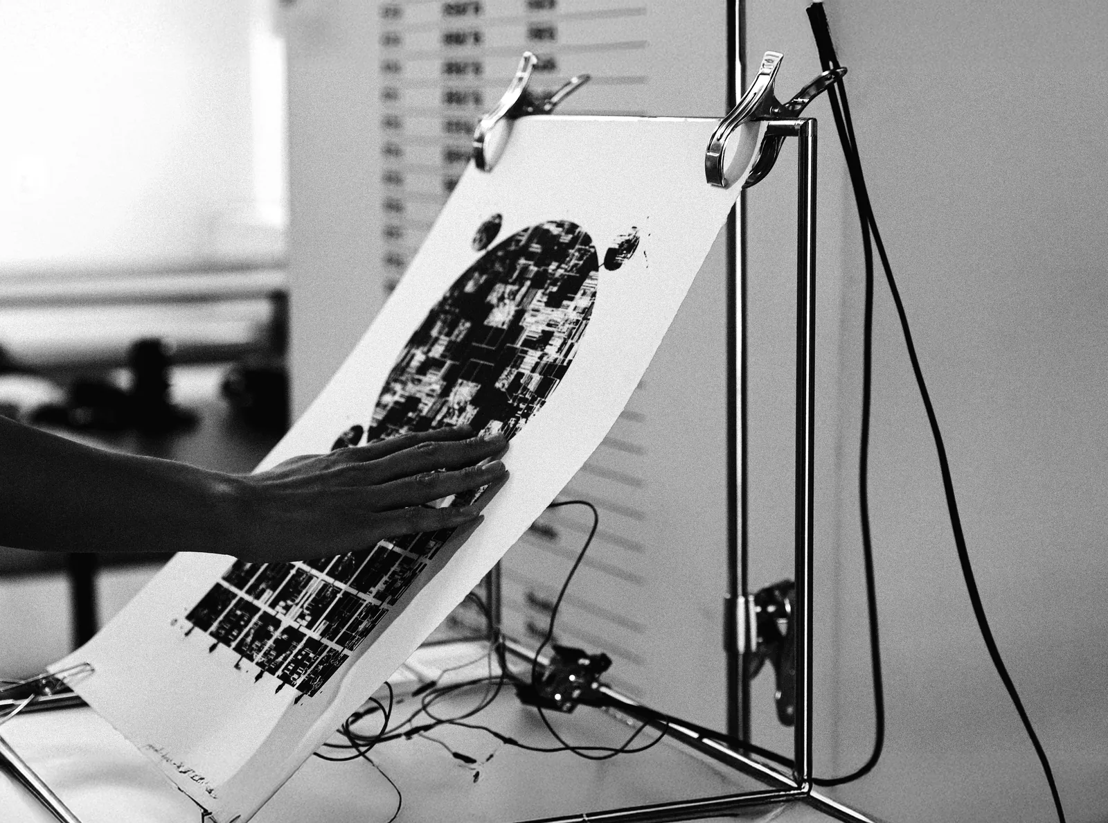 The whole setup: a silkscreen poster clamped to a lab stand, a hand pressed to its printed surface, cables running from the sheet down to equipment on the table.
