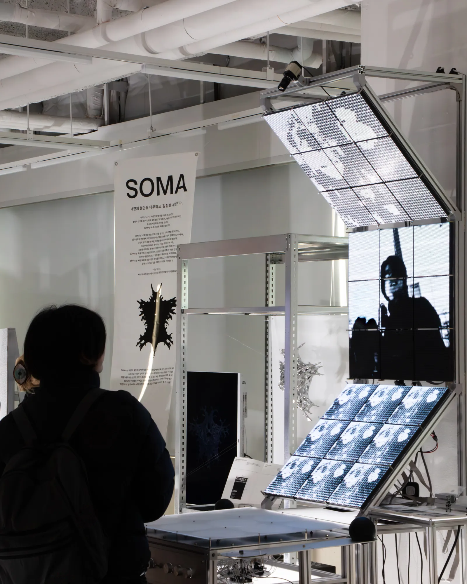 A visitor standing in front of the work, watching a figure appear across the middle display panel.