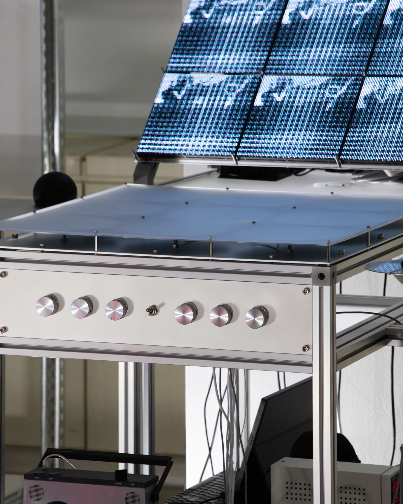 Close view of the control panel: six machined aluminium knobs and one toggle switch on a brushed front plate, under a satin acrylic tabletop.
