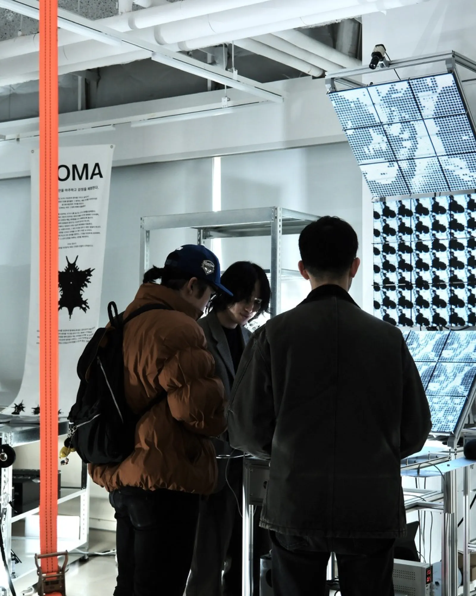 Three visitors gathered at the table of the work, one reaching toward the controls, the panels dense with dithered black-and-white pattern.